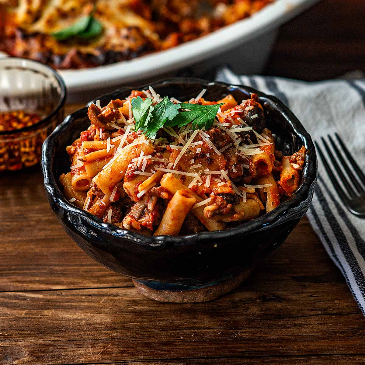 A bowl of Baked Ziti topped with shredded parmesan and garnished with fresh Italian Parsley.