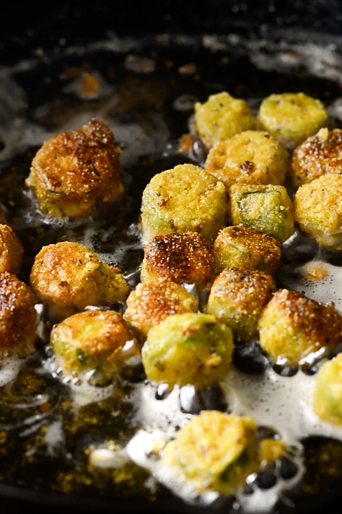 Breaded okra being fried in a cast iron skillet.