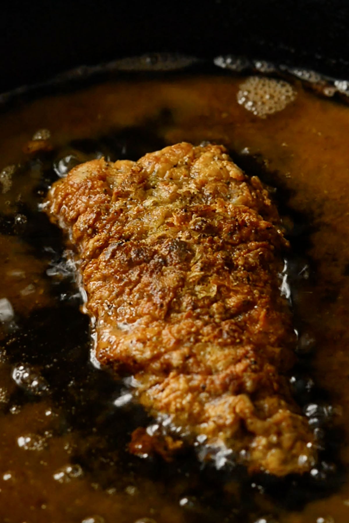 Chicken Fried Steak frying in a cast iron skillet with hot vegetable oil.