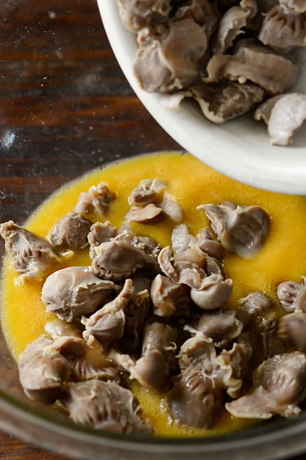 Boiled chicken gizzards in a bowl of egg and hot sauce wash.