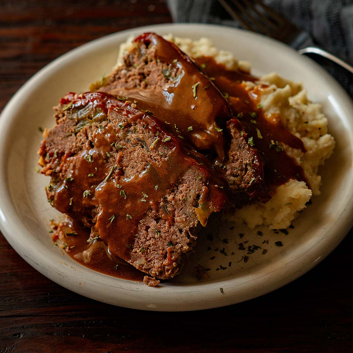 Two slices of Meatloaf served with mashed potatoes and topped with brown gravy.