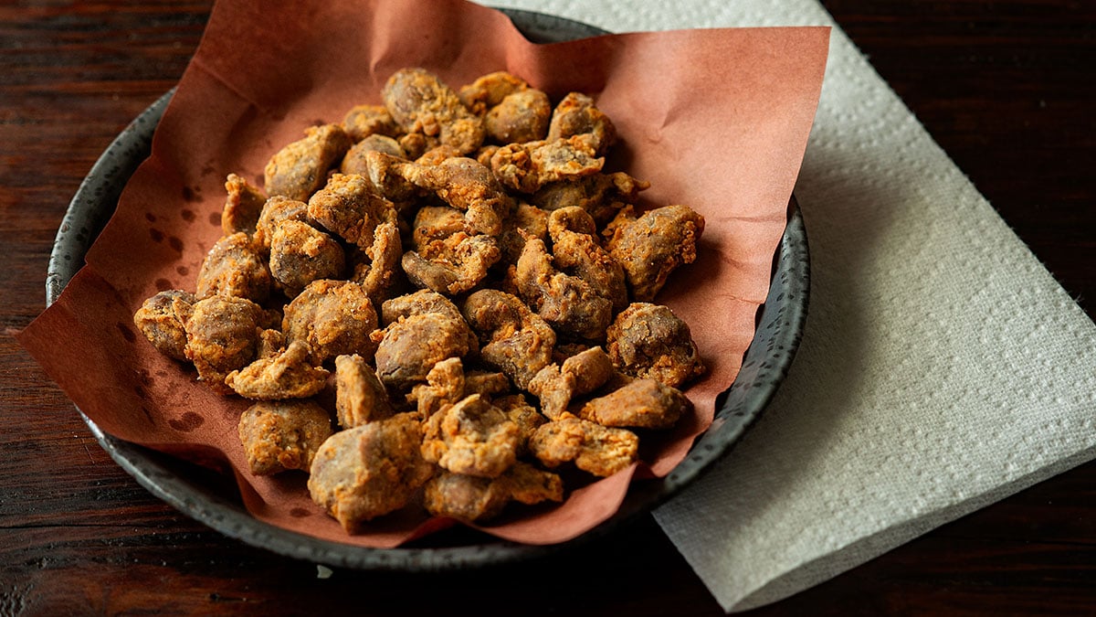 Deep fried chicken gizzards served on a peach butcher paper lined plate with paper towels on the side.