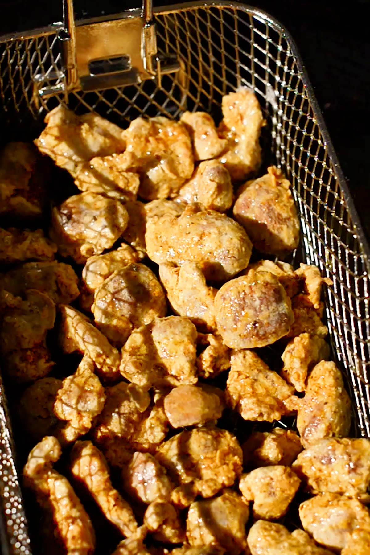 Breaded chicken gizzards being fried in a deep fryer.