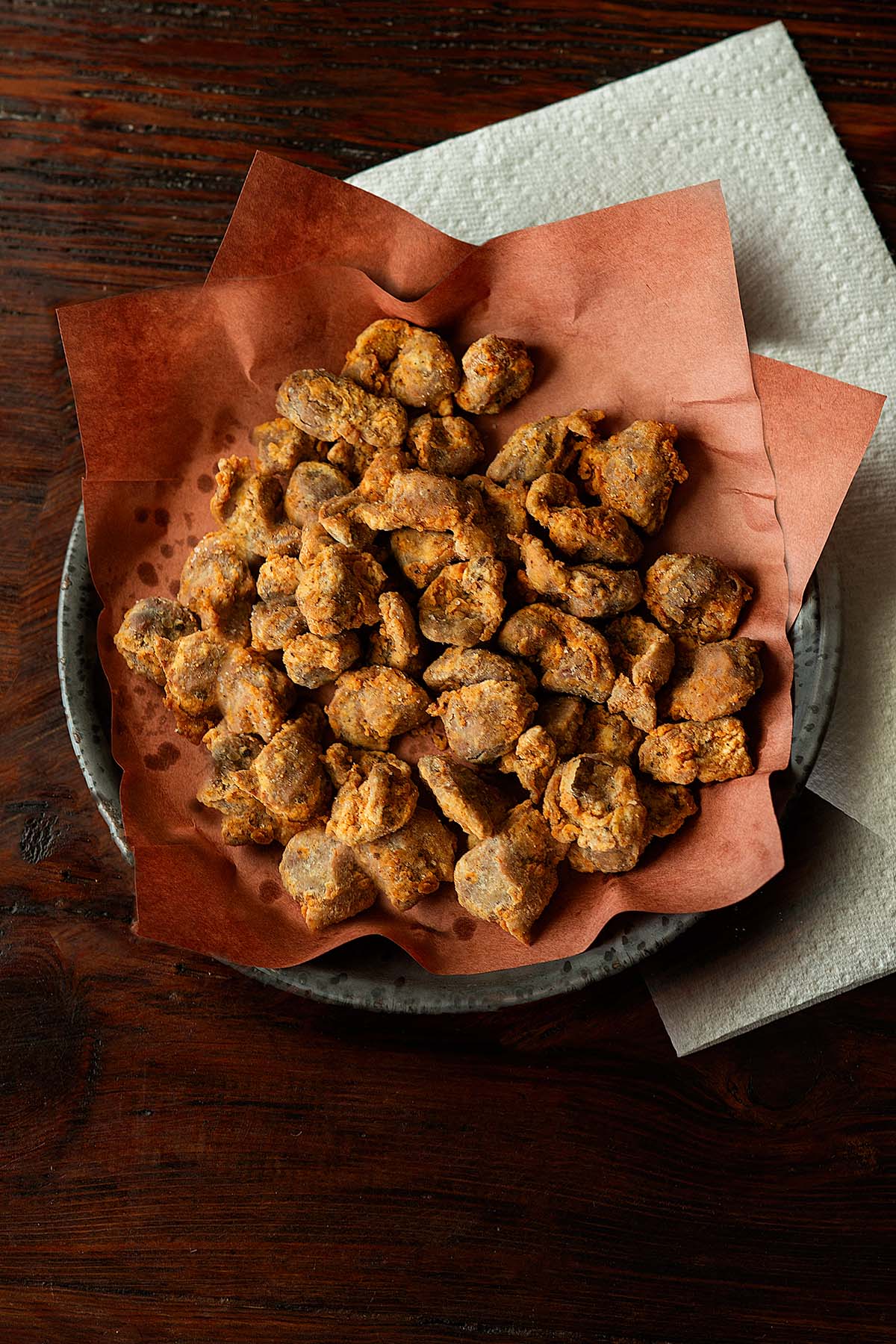 Fried chicken gizzards served on a butcher paper lined plate with paper towels on the side.