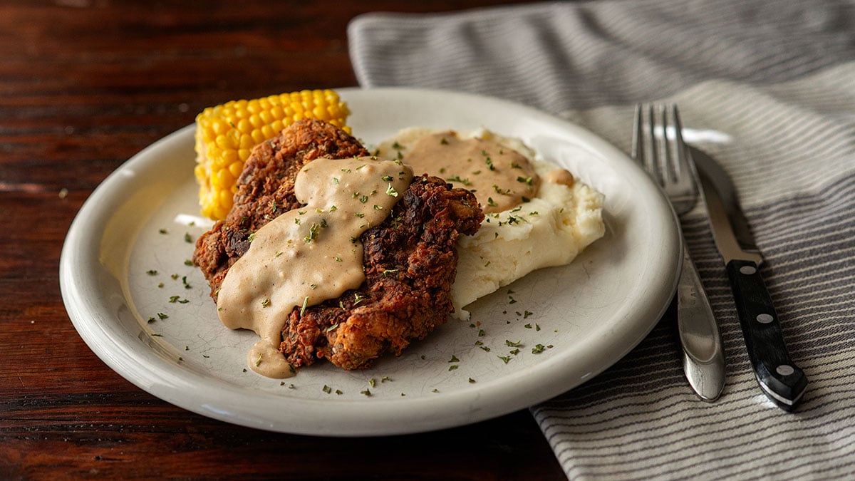 Chicken fried steak, mashed potatoes, corn on the cob, and cream gravy plated and served.