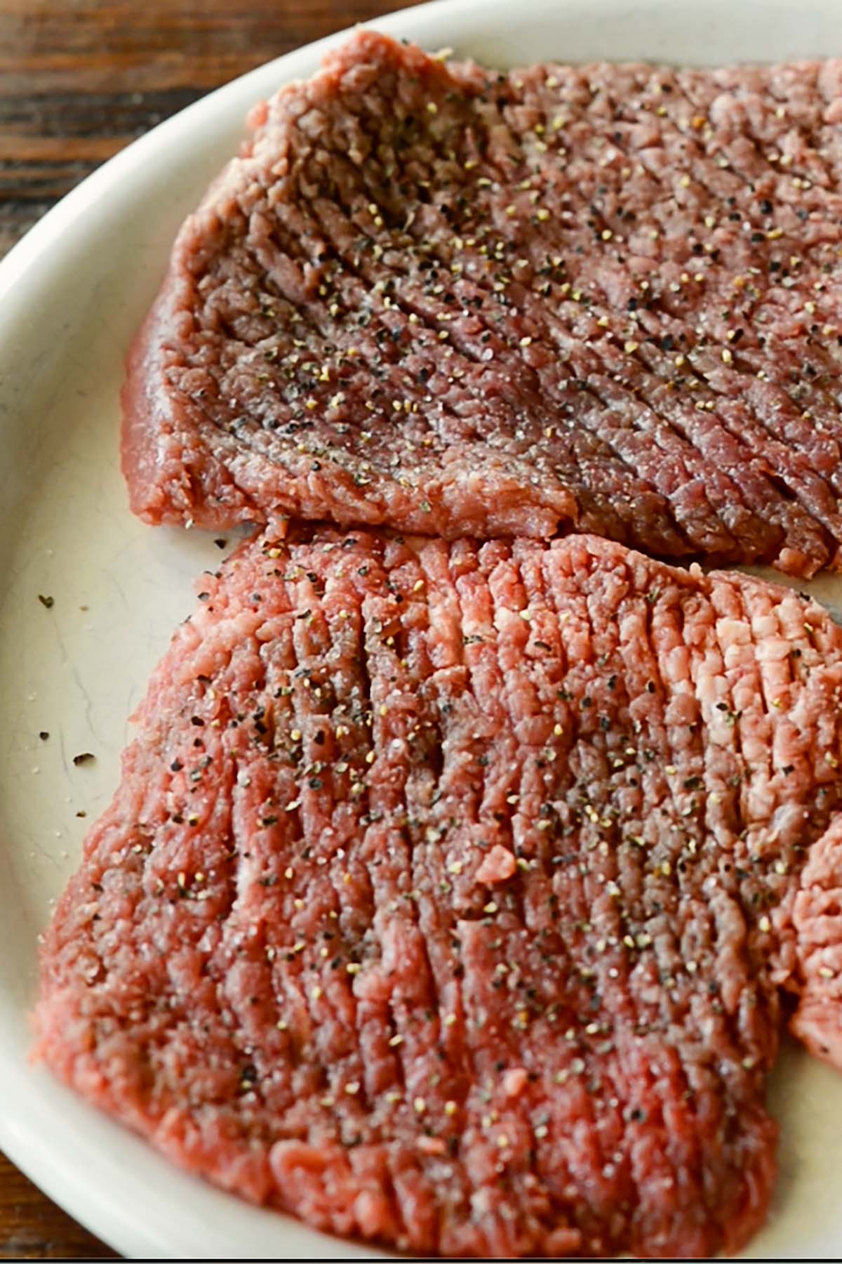Cube Steak seasoned with salt and pepper on a plate.