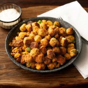 Southern fried okra served on a metal plate with a paper towel, fork, and side of ranch dressing.