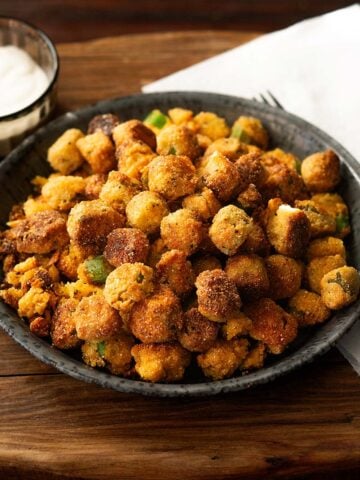 Southern fried okra served on a metal plate with a paper towel, fork, and side of ranch dressing.