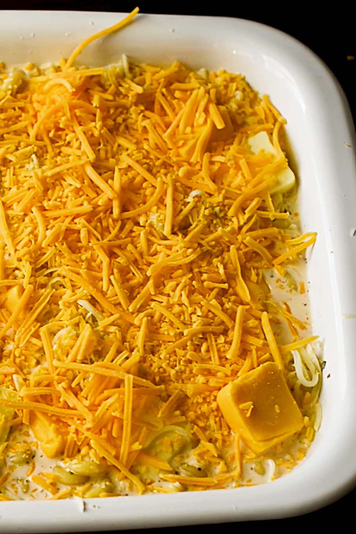 Shredded cheddar cheese spread evenly over the top of a creamy macaroni mixture in a baking dish.