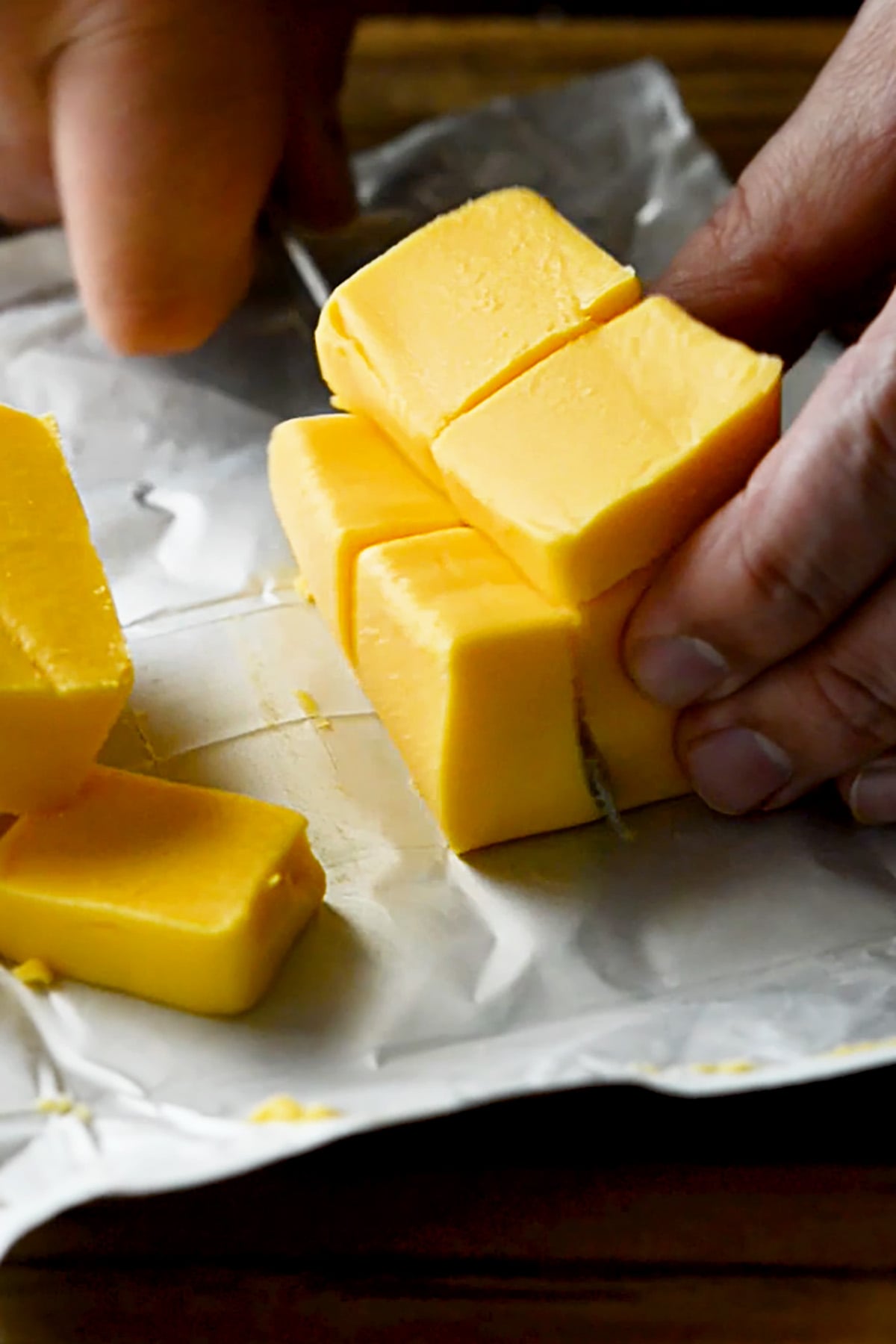 Velveeta Cheese being cubed on a wood cutting board.