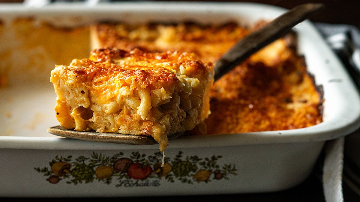 Southern baked mac and cheese with a wooden spatula in a vintage baking dish.