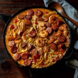 Cajun Shrimp and Sausage Pasta in a cast Iron skillet on a wooden table with a wooden spoon and towel.