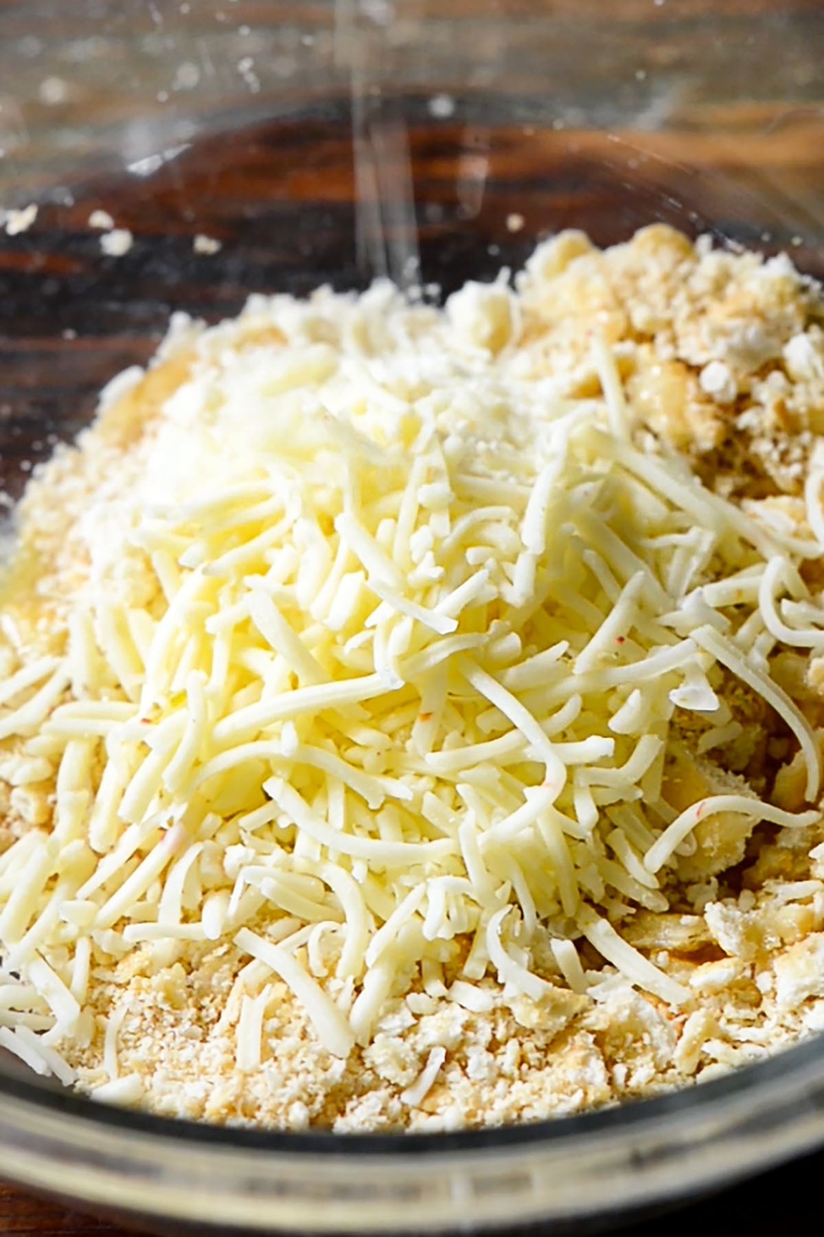 Shredded Pepper Jack cheese being added to a bowl of crumbled Ritz crackers.
