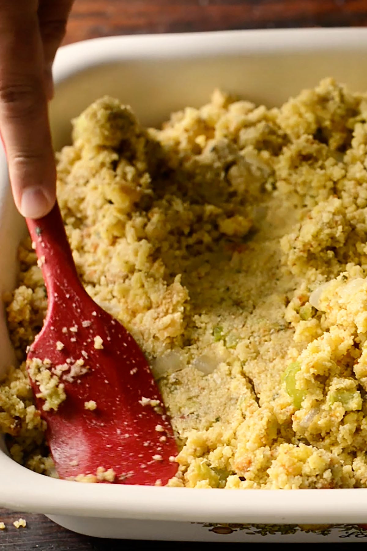 Southern cornbread dressing being pressed down in a baking dish.