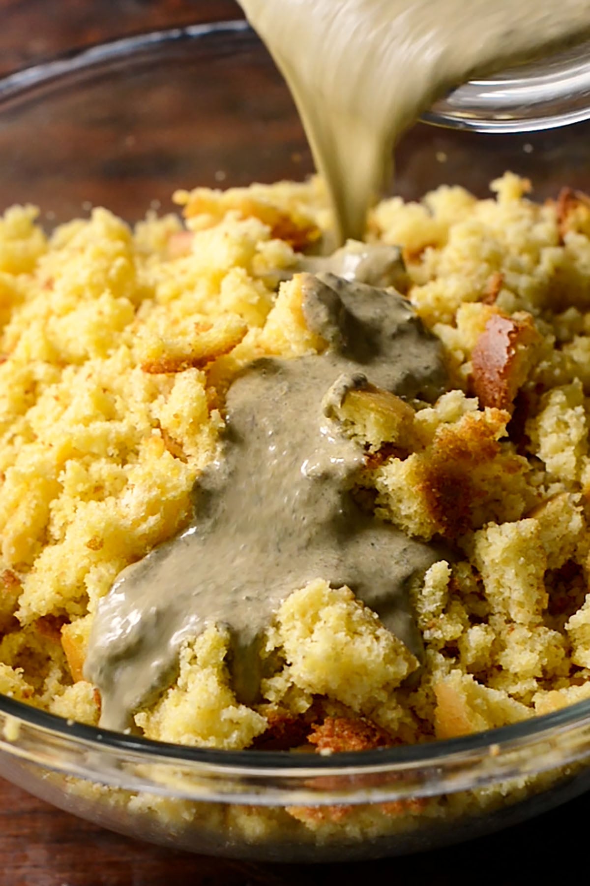 A seasoned egg and cream mixture being poured over crumbled cornbread.