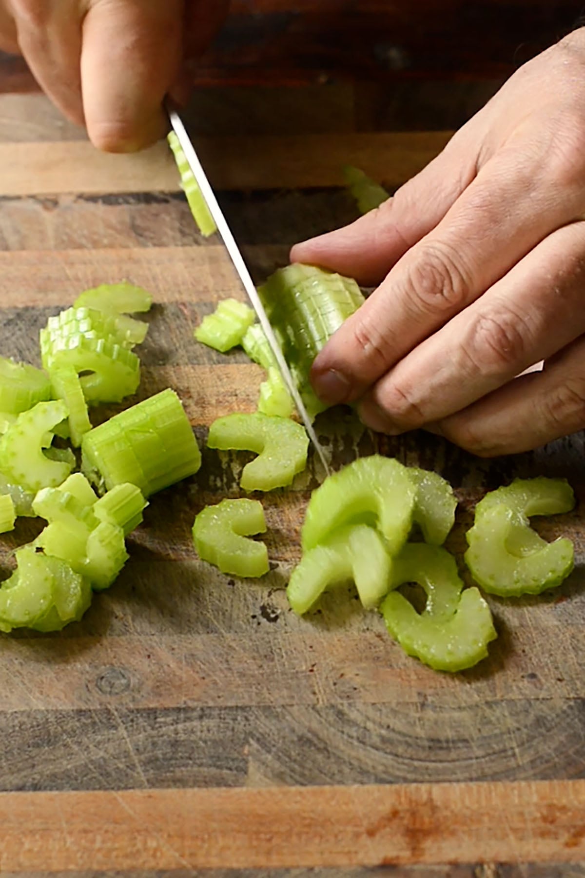 Celery being diced on a wooden cutting board.