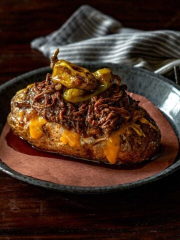 Mississippi served on a baked potato with cheese and topped with two pepperoncini peppers.