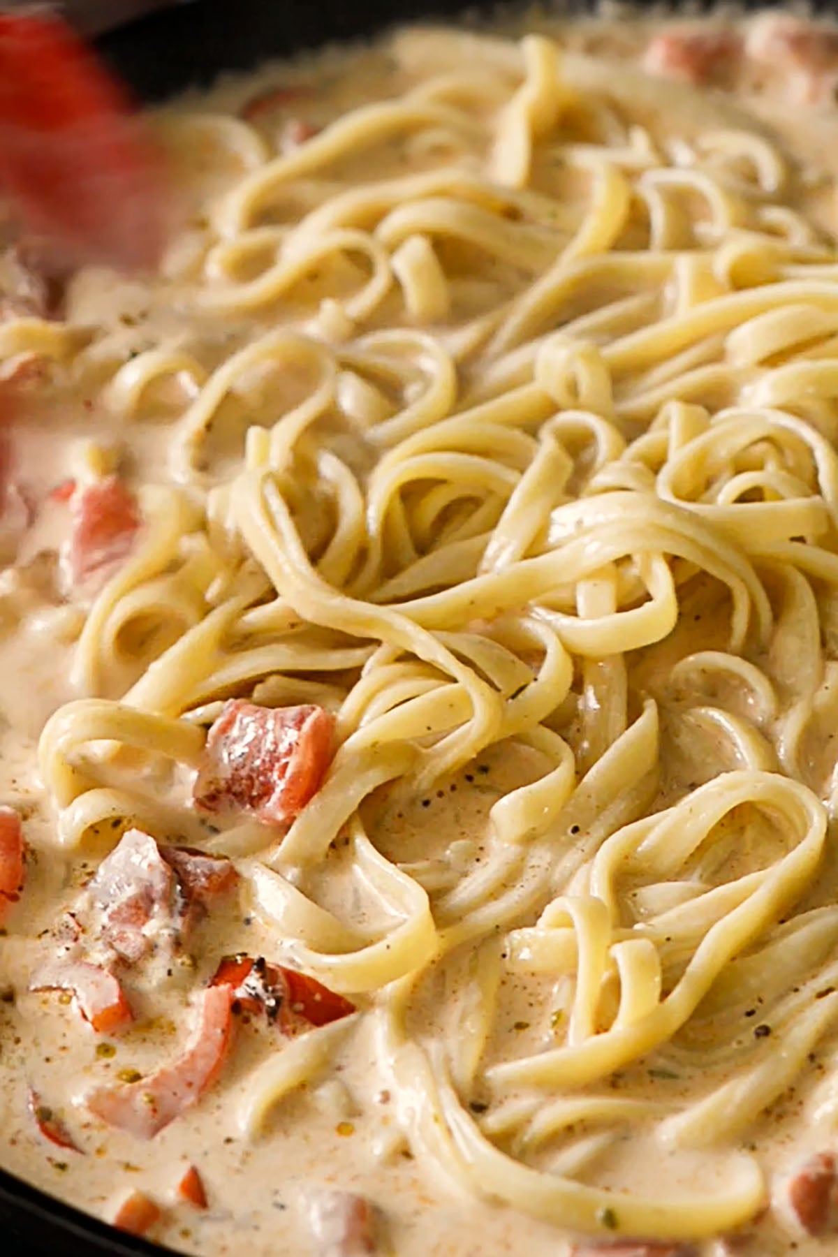 Cooked fettuccini being tossed in a creamy cheesy cajun sauce. 