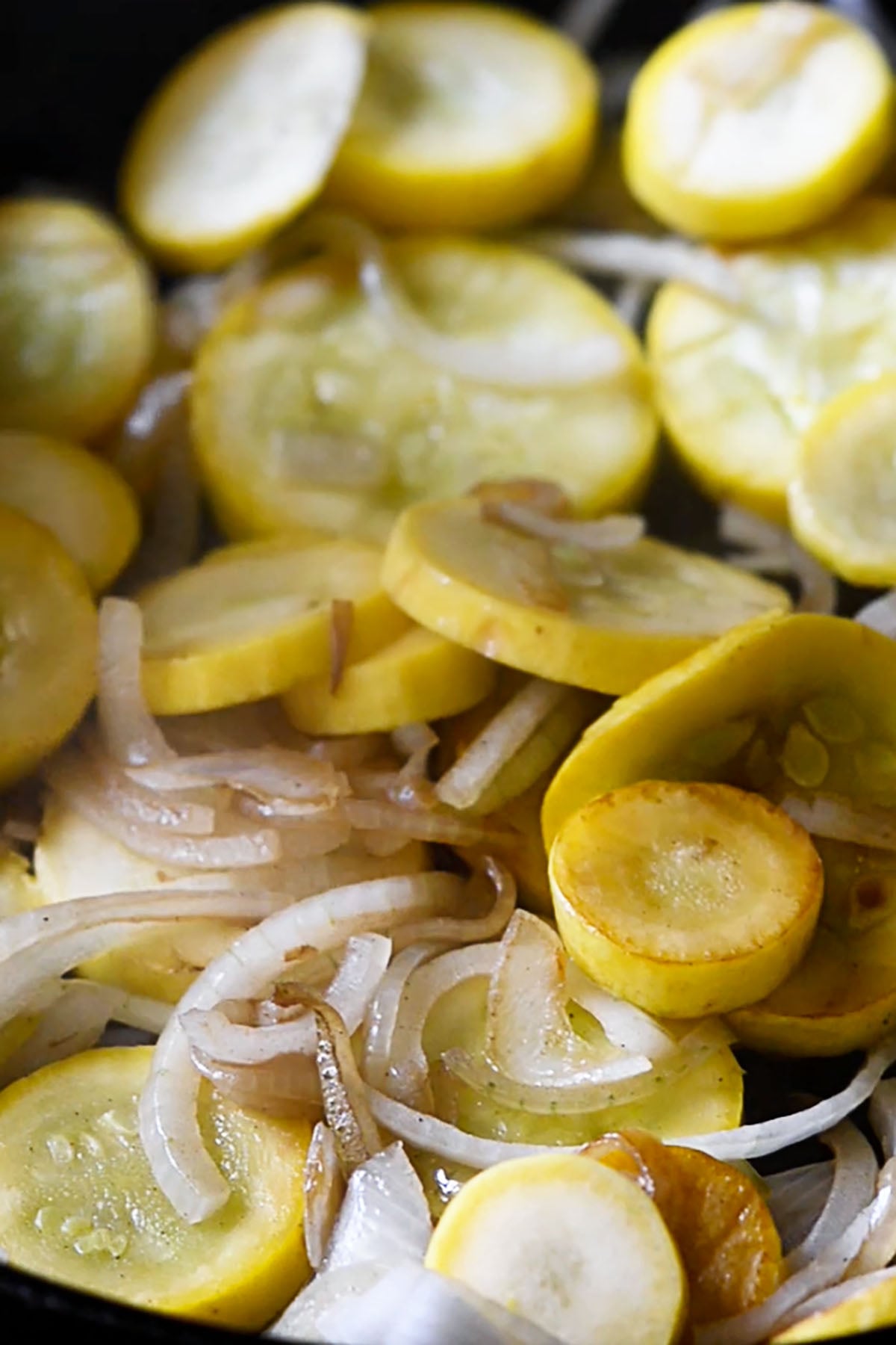 Sliced squash and onions cooking in a cast iron skillet.