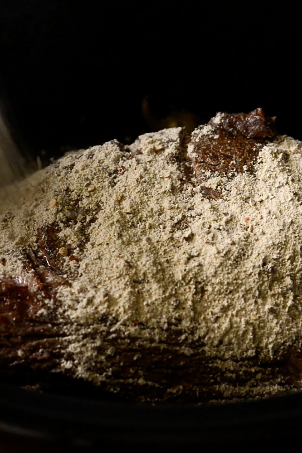 A seared chuck roast in a slow cooker covered with powdered ranch dressing seasoning and Italian beef au jus seasoning.