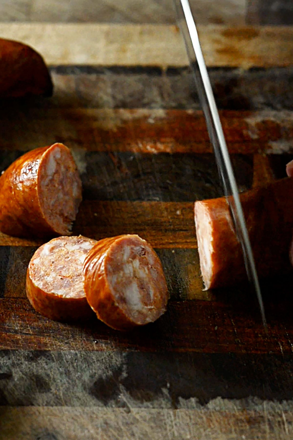 Sausage being sliced on a wooden cutting board.