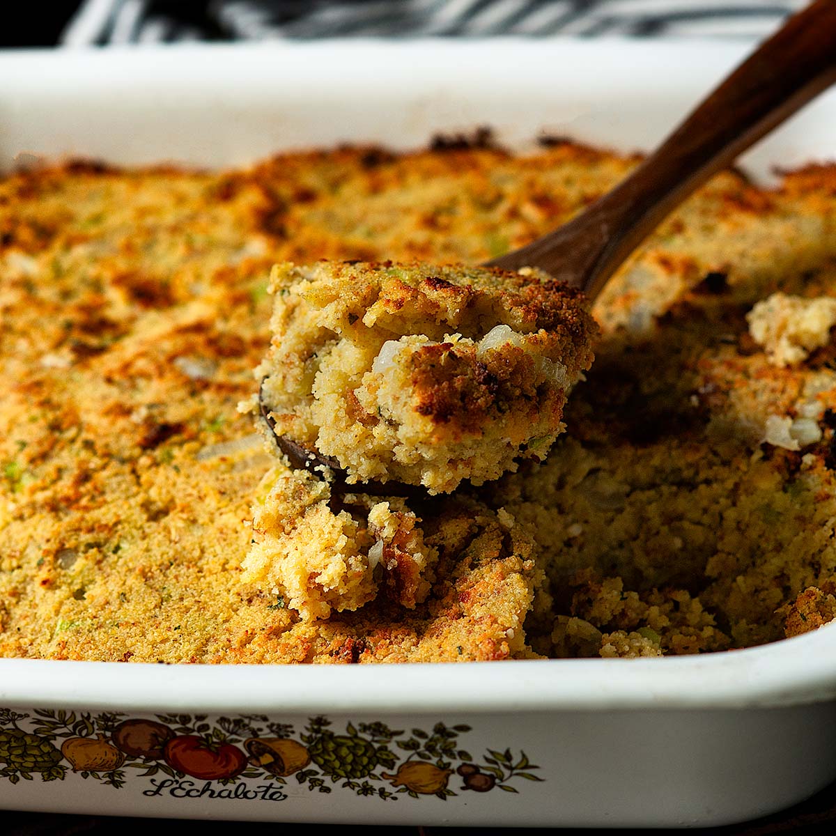 Southern Cornbread Dressing served in a vintage white baking dish with a wooden spoon full.