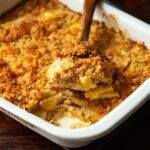 A wooden spoonful of Southern Squash Casserole in a vintage white baking dish.