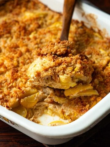 A wooden spoonful of Southern Squash Casserole in a vintage white baking dish.