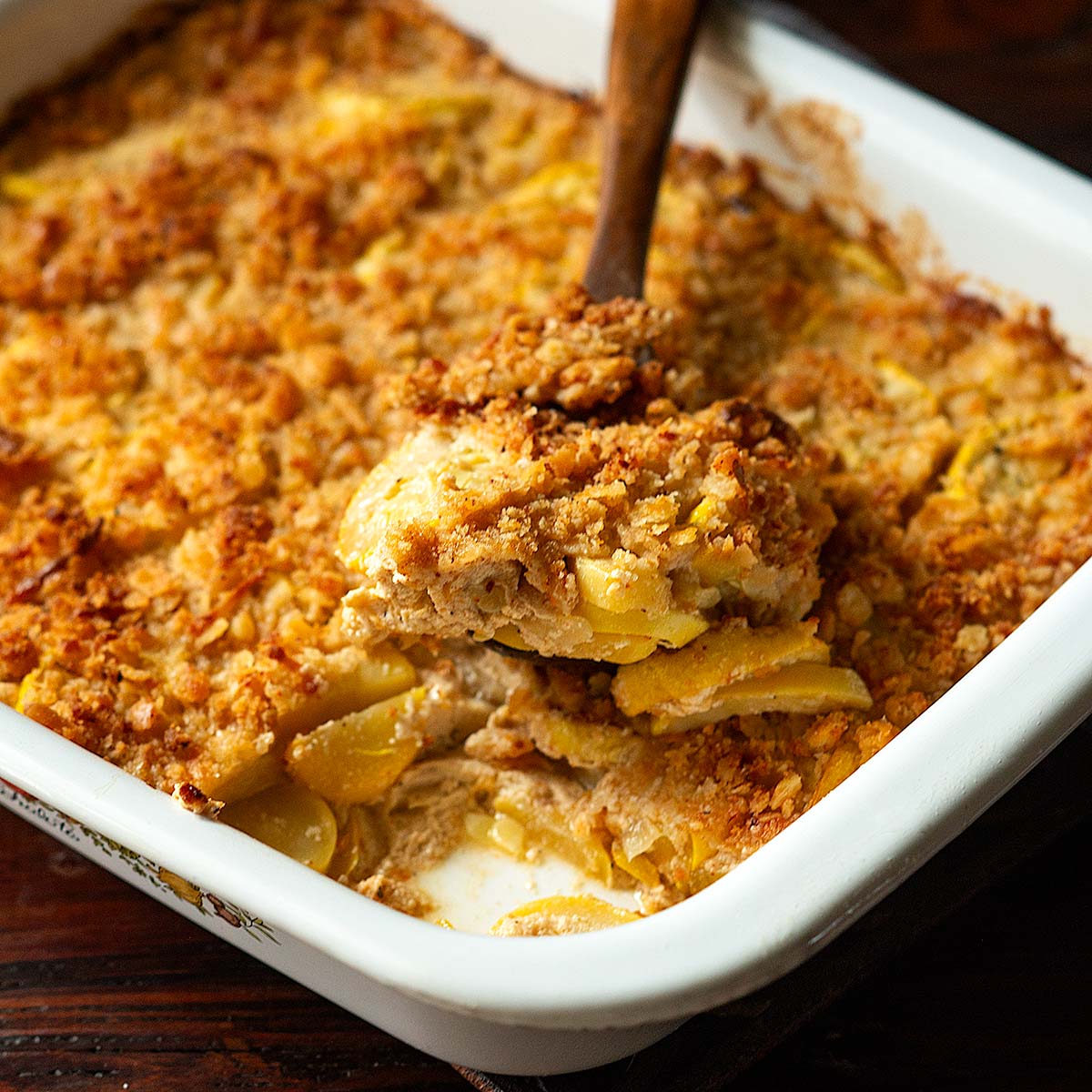 A baking dish full of Southern Squash Casserole with a wooden spoonful ready to serve.