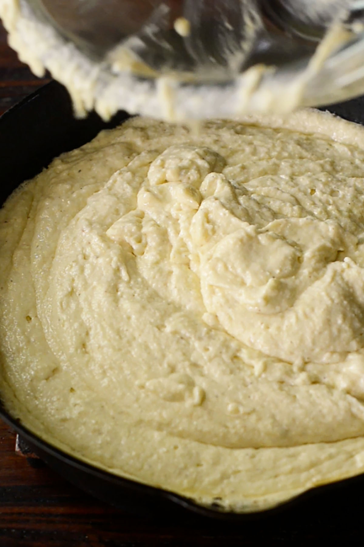 Southern cornbread batter being poured into a hot cast iron skillet. 