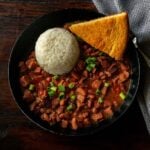 Classic Louisiana Red Beans and Rice served in a deep black dish with fresh cornbread and garnished with sliced green onions.