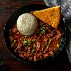 Classic Louisiana Red Beans and Rice served in a deep black dish with fresh cornbread and garnished with sliced green onions.