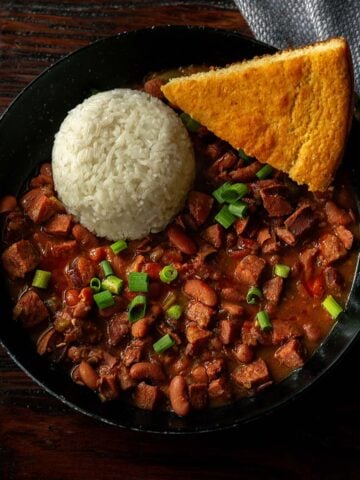 Classic Louisiana Red Beans and Rice served in a deep black dish with fresh cornbread and garnished with sliced green onions.