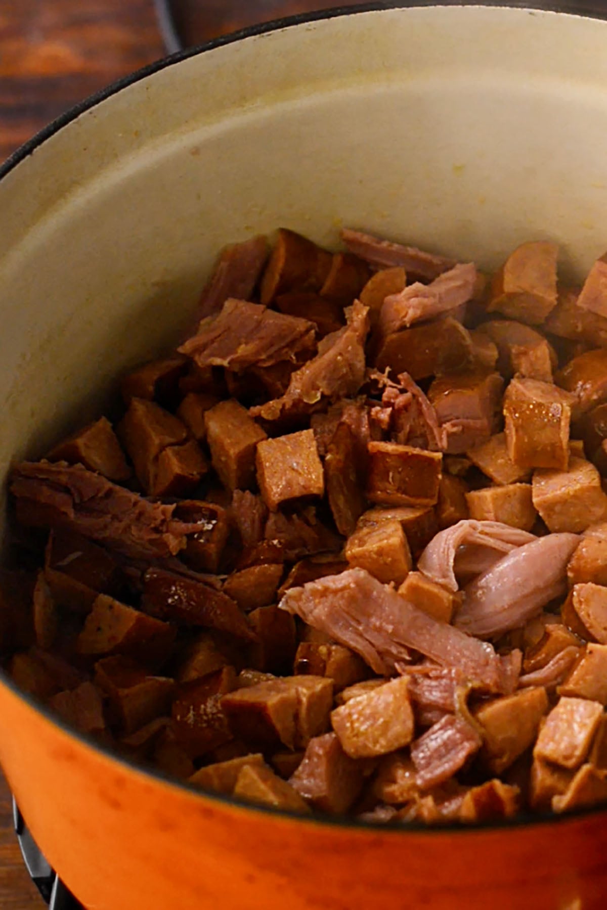 Cubed Andouille sausage and smoked turkey pulled from a drumstick cooking in a dutch oven.