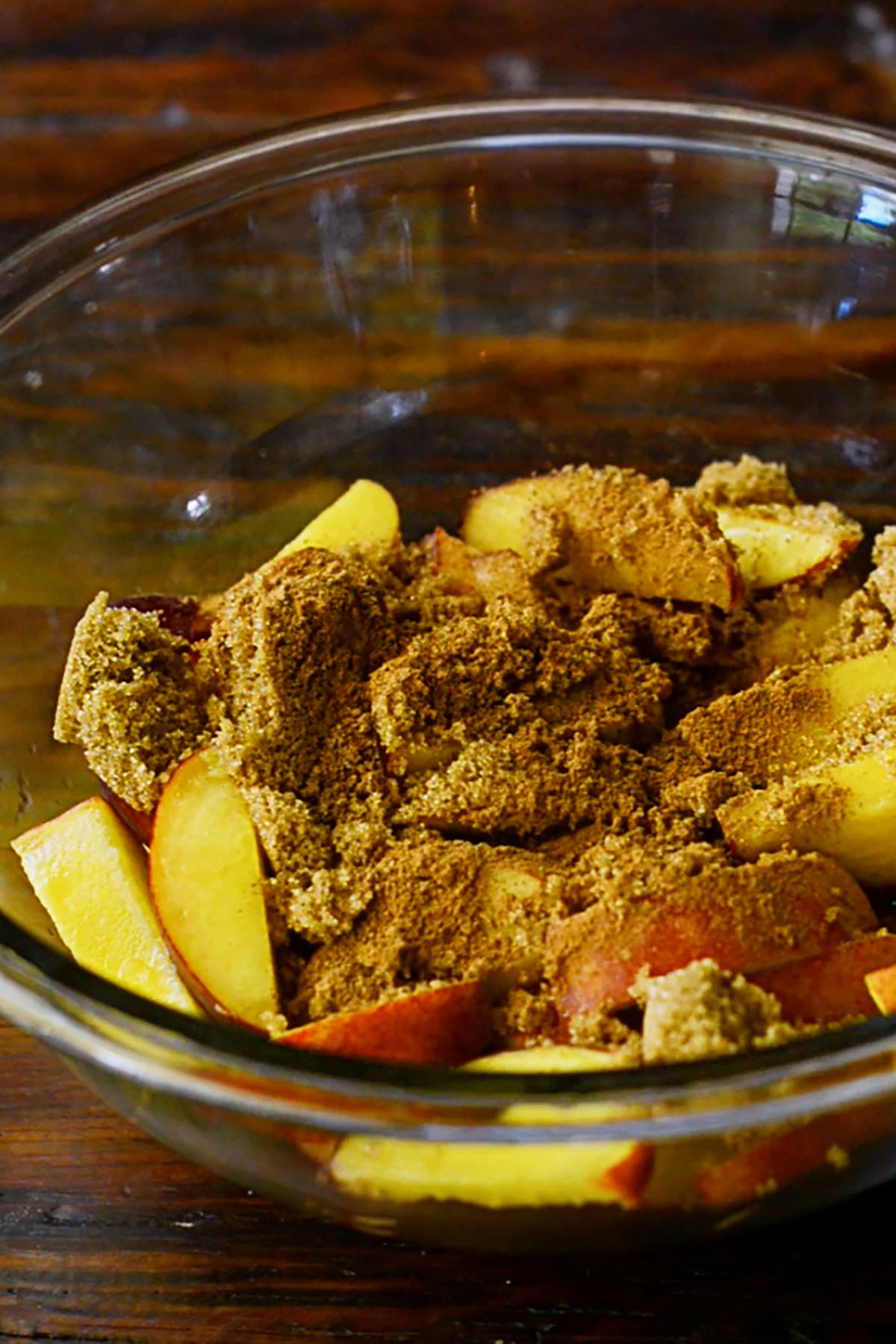 Peach cobbler seasoning spread over fresh peaches in a glass mixing bowl.