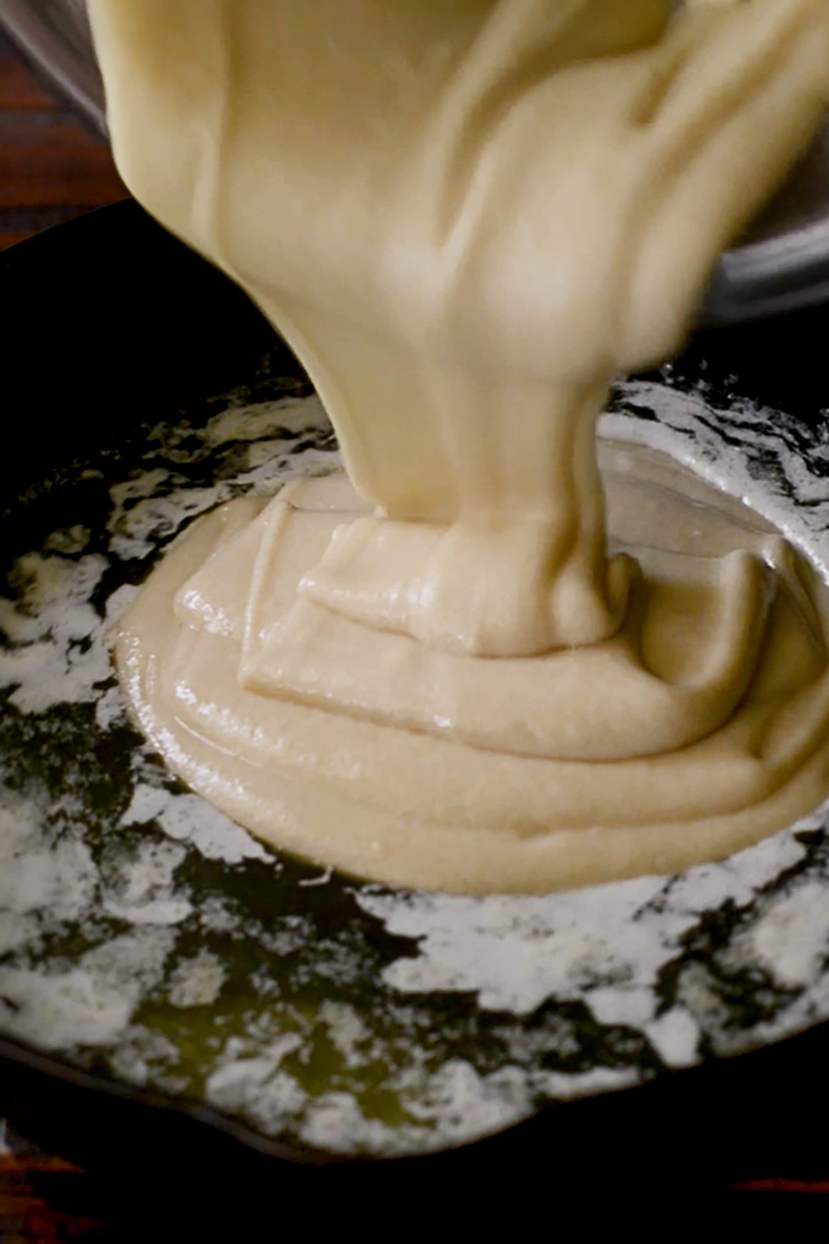 peach cobbler batter being poured into melted butter in a cast iron skillet.