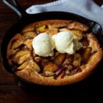 Southern peach cobbler in a cast iron skillet served with two scoops of vanilla bean ice cream on top.