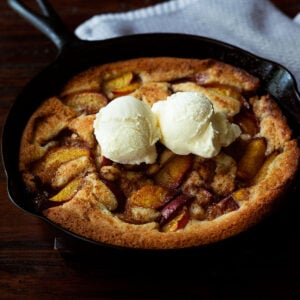 Southern peach cobbler in a cast iron skillet served with two scoops of vanilla bean ice cream on top.