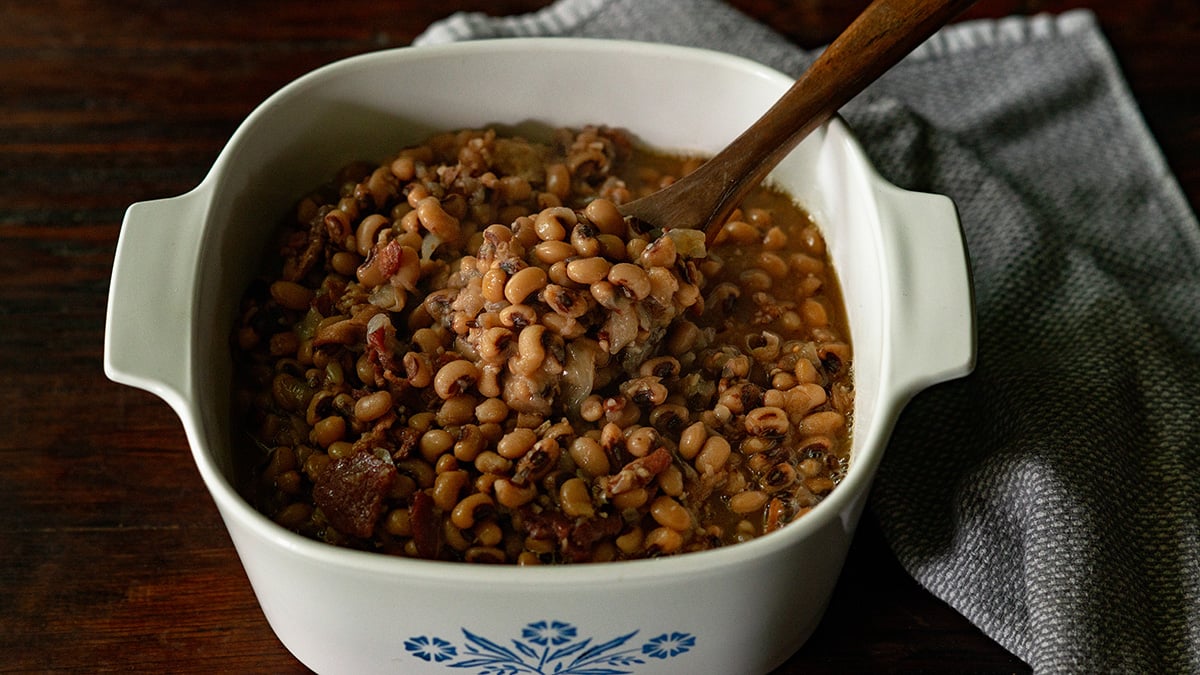 Black Eyed Pease served in a vintage white baking dish with a wooden spoon scooping in the center.