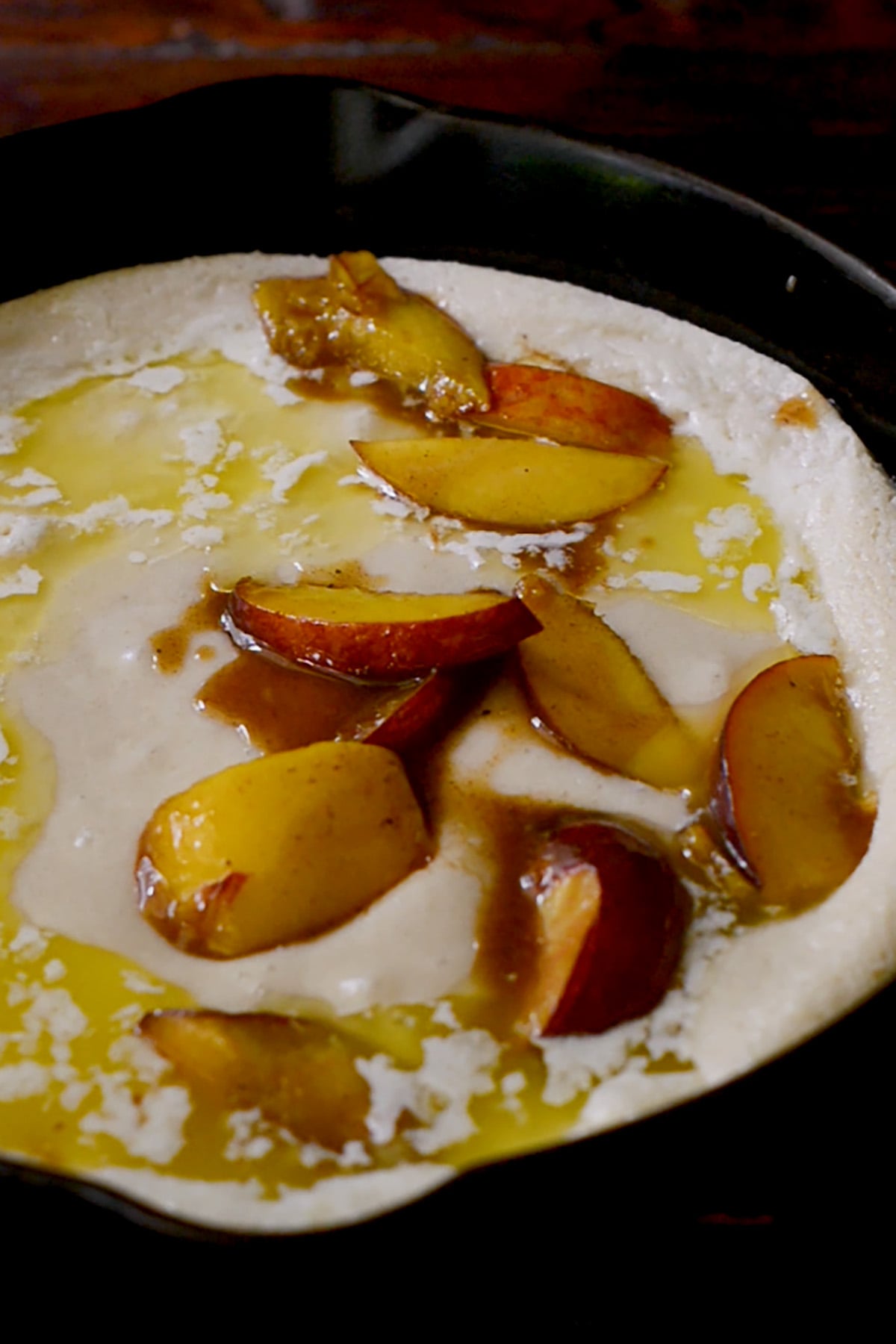 Peach cobbler filling being poured over the top of a southern peach cobbler base.