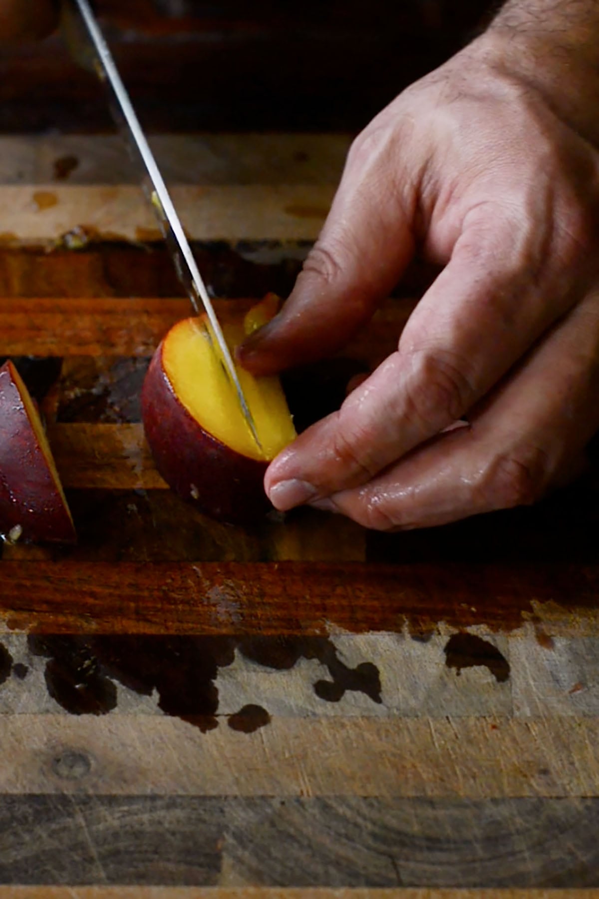 A peach being sliced on a wood cutting board.