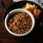 Black-Eyed Peas served in a white bowl with a black plate and fresh baked cornbread on the side.