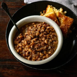 Black-Eyed Peas served in a white bowl with a black plate and fresh baked cornbread on the side.