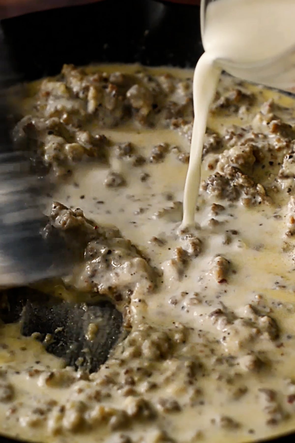Milk being poured into a cast iron skillet full of southern sausage gravy.