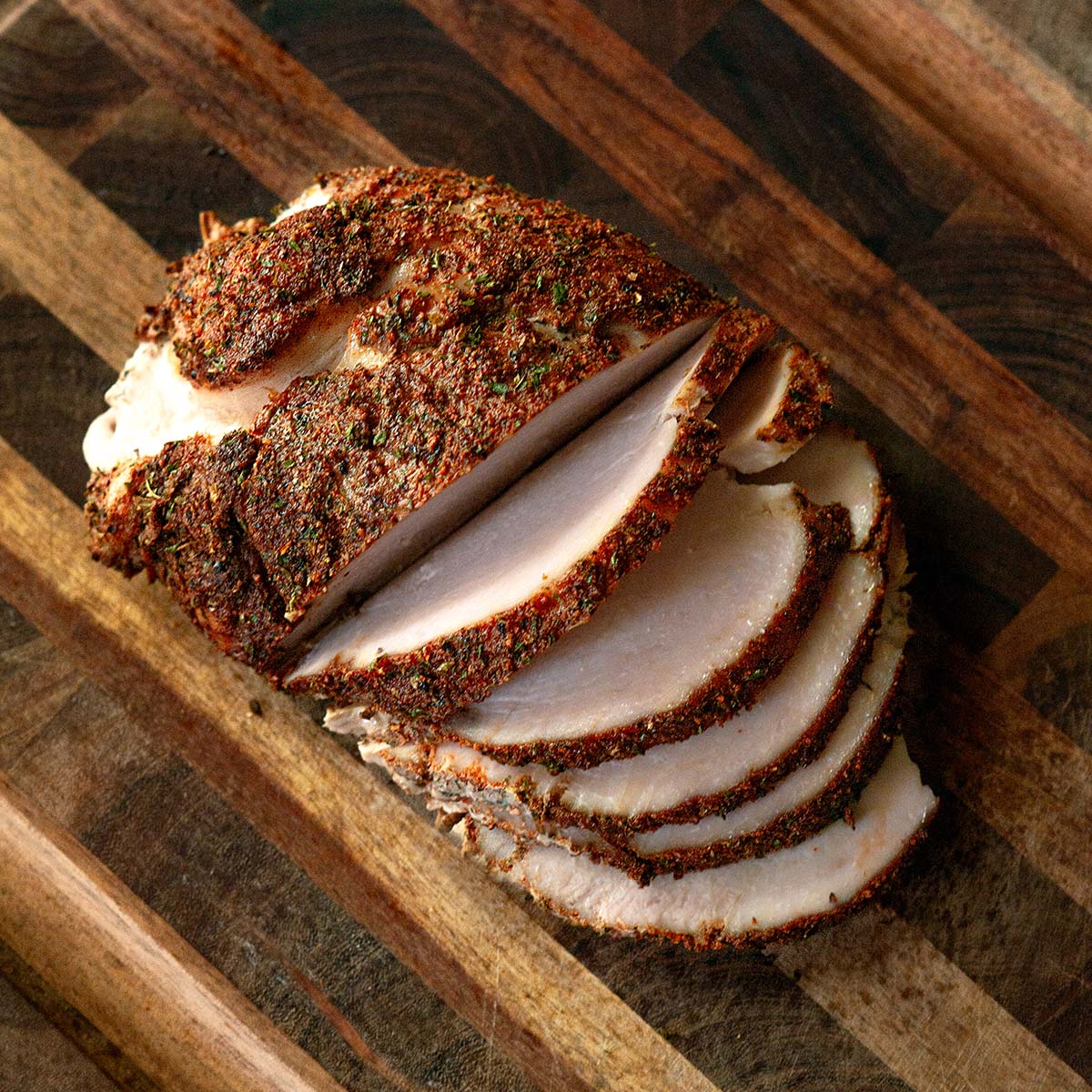 A smoked turkey breast seasoned and sliced on a wood cutting board.