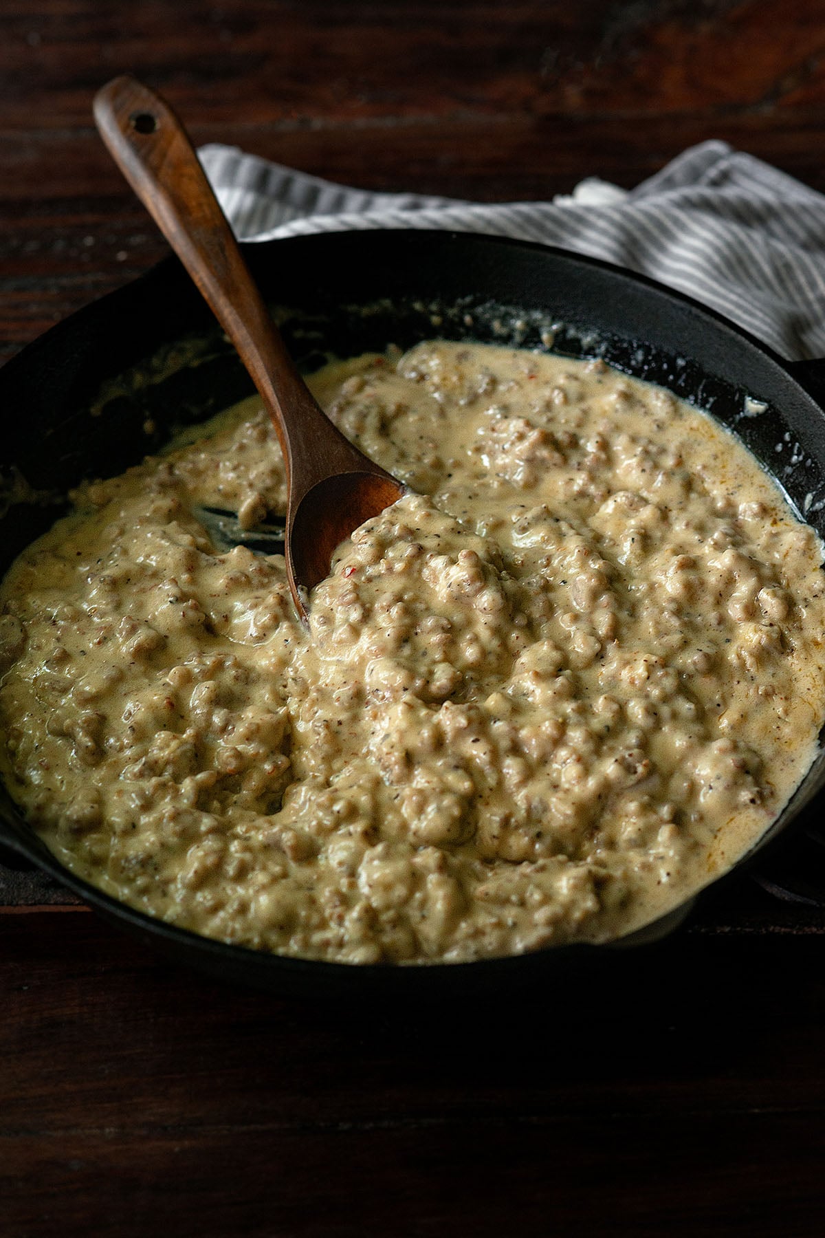 Southern sausage gravy served in a cast iron skillet with a wooden spoon.