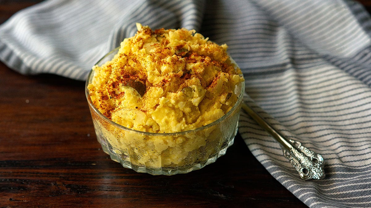 Homemade Southern potato salad served in a clear dish and topped with paprika.