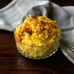 Southern potato salad served in a clear bowl on a wood table and topped with a sprinkle of paprika.