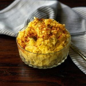 Southern potato salad served in a clear bowl on a wood table and topped with a sprinkle of paprika.