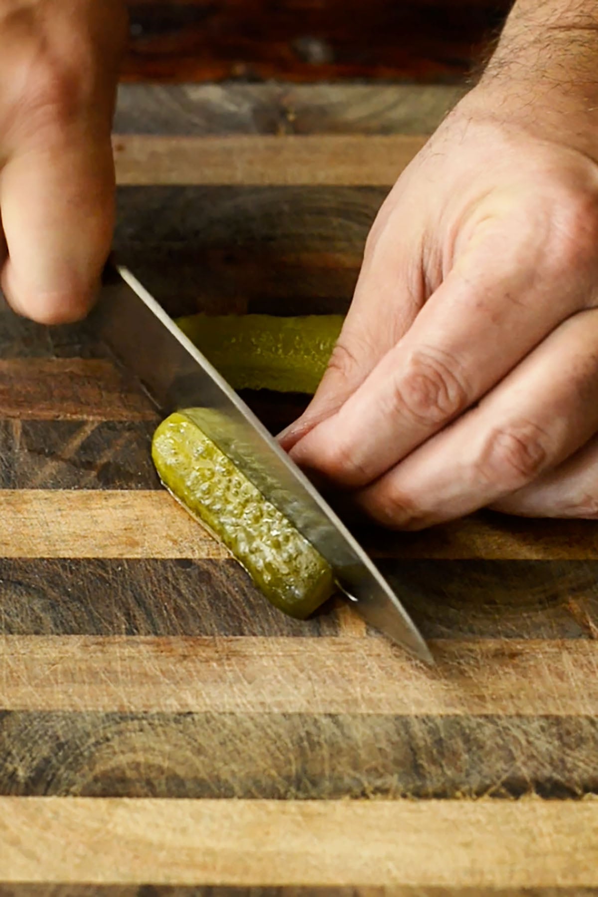 A dill pickle being sliced on a wood cutting board.